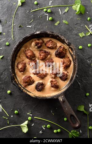 Skandinavisches Komfortessen. Fleischbällchen in Soße in schwarzer Pfanne auf schwarzem Hintergrund Draufsicht Kopierraum Stockfoto