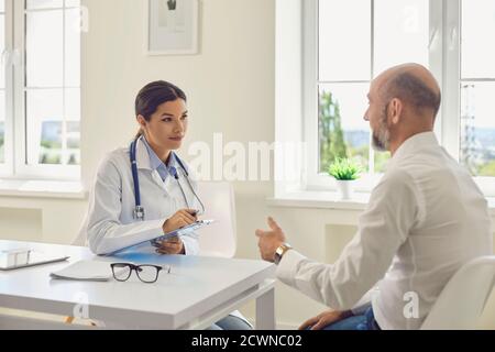 Männlicher Rentner spricht mit dem Arzt am Schreibtisch im Büro des Krankenhauses. Stockfoto