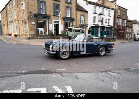 Paar in einem offenen Triumph TR6 Sportwagen fahren durch das Yorkshire Dales Dorf Masham, Engalnd. Stockfoto