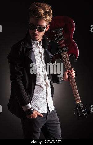 Seitenansicht eines jungen Rockers, der seine Gitarre auf hält Schulter und Blick zurück auf schwarzen Studio-Hintergrund Stockfoto