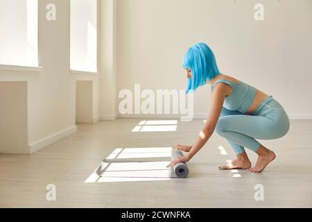 Junge sportliche Frau verteilt eine Yogamatte auf dem Boden am Morgen vor dem Training. Stockfoto