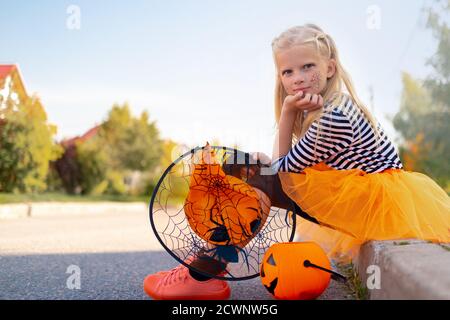 Halloween Kinder. Lächelndes Mädchen in Hexenhut mit Kürbis Süßigkeiten Eimer. Lustige Kinder in Karnevalskostümen im Freien Stockfoto