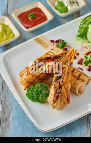 Türkische tantuni in weißem Teller auf Holztisch, serviert mit verschiedenen Saucen und Chips. Stockfoto