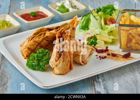 Türkische tantuni in weißem Teller auf Holztisch, serviert mit verschiedenen Saucen und Chips. Stockfoto