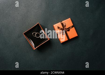 Eheringe in einer Box auf dunklem Hintergrund. Offene braune Schachtel mit den Ringen der Braut und des Bräutigams. Hochzeitskonzept. Draufsicht, flaches Layout Stockfoto