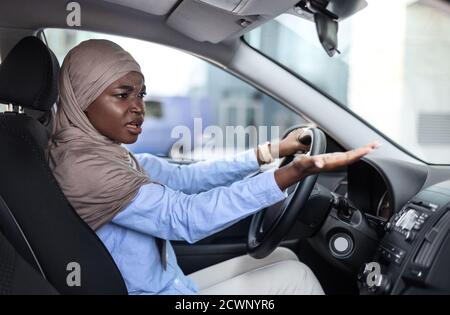 Gestresste schwarze muslimische Frau argumentiert mit jemandem während der Fahrt Auto Stockfoto