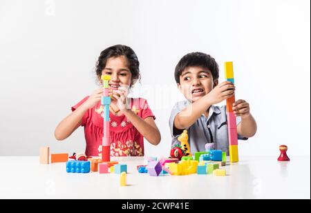 Nette kleine indische asiatische Kinder spielen mit bunten Kunststoff-Spielzeug Oder Blöcke beim Sitzen am Tisch oder isoliert über weiß Hintergrund Stockfoto