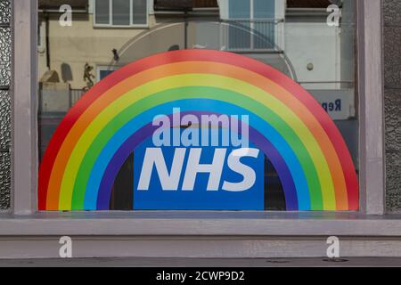 Ein Regenbogen- und NHS-Schild im Schaufenster eines Ladens, das die Unterstützung des NHS während der Coronavirus-Pandemie zeigt Stockfoto