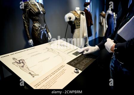 30. September 2020, Berlin: Ein Besucher berührt mit einem Handschuh eine Stoffprobe des Abendkleides aus silbernem Lamé aus dem Film Lili Marleen von Regisseur Werner Fassbender für die Schauspielerin Hanna Schygulla in der Ausstellung 'Hautnah. Die Filmkostüme von Barbara Baum' in der Deutschen Kinemathek - Museum für Film und Fernsehen. Ab 01.10. 2020 bis 03.05.2021 werden über 40 originale Filmkostüme aus fünf Jahrzehnten Kostümdesign gezeigt. Foto: Britta Pedersen/dpa-Zentralbild/dpa - ACHTUNG: Nur zur redaktionellen Verwendung im Zusammenhang mit der aktuellen Berichterstattung und nur bei vollständiger Erwähnung der obigen Credi Stockfoto