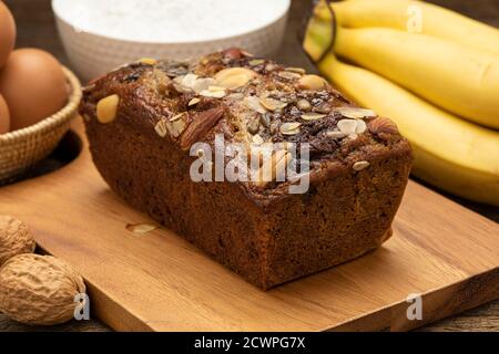 Nahaufnahme Bananenkuchen werden auf einem Holztablett auf einem Holztisch mit Bananen, Eiern, Mehl als Hintergrund platziert. Stockfoto