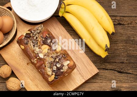 Bananenkuchen werden auf einem Holztablett auf einem Holztisch platziert, mit Bananen, Eiern, Mehl als Hintergrund. Draufsicht. Stockfoto
