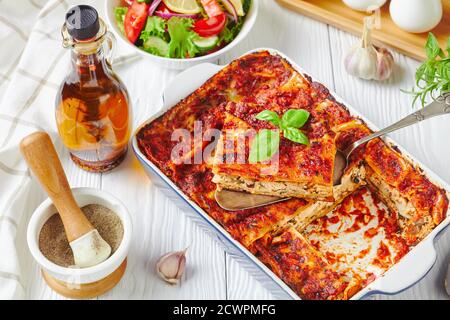 Milchfreie Lasagne mit festem Tofu, Pilzen, Passata-Sauce in einer Backform serviert mit einem frischen Salat aus Salat, Tomaten, Gurken, roten Zwiebeln und Bas Stockfoto