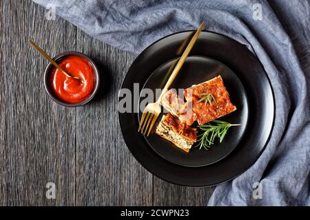 Amerikanischer Tofu Spinat vegane Lasagne mit Champignon und Tomaten vegetarisch bolognese serviert auf einem schwarzen Teller mit Gabel und frisch Rosmarin auf einem dunklen rus Stockfoto