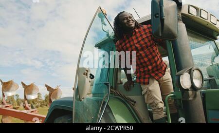 Junger afrikanischer Bauer, der auf dem Bauernhof aus dem grünen Traktor ausfährt. Hochwertige Fotos Stockfoto