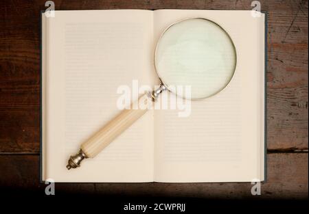 Retro offenes Buch mit Lupe auf alten Holztisch Stockfoto