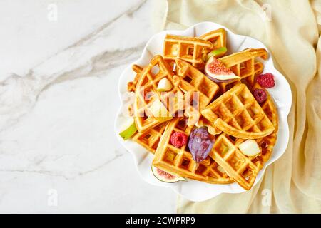 Belgische Waffeln mit frischen Beeren, Birnen, Feigen auf einem blauen Teller auf einem Marmortisch, flach liegend, Freiraum Stockfoto
