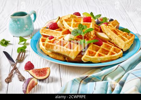 Belgische Waffeln mit frischen Beeren, Birnen, Feigen auf einem blauen Teller auf einem weißen Holztisch Stockfoto