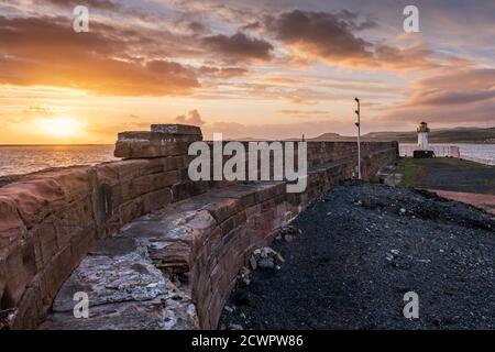 Ardrossan Hafenmauer und Leuchtturm bewachen den Hafeneingang zum Ardrossan Hafen am Firth of Clyde bei Sonnenuntergang, North Ayrshire, Schottland. Stockfoto