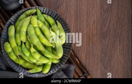 Frisch gekochte gekochte Edamame in einem Teller auf Holztablett und Tischhintergrund, Protein-Food-Konzept. Stockfoto