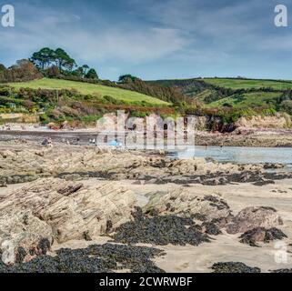 Eine Strandszene in Talland Bay, Cornwall, England, Urlauber genießen die Herbstsonne und ein Bad im Meer. Ein Strand aus Naturstein und Sand. Stockfoto