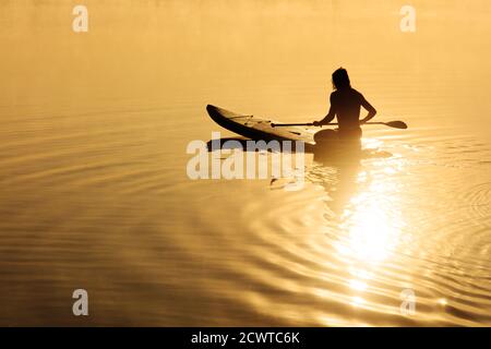 Mann sitzt auf dem Brett und mit Paddel zum Schwimmen Stockfoto