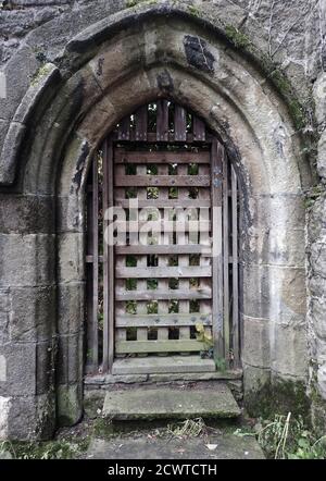 Eine romanische gotische Steingewölbe Tür in Whalley Abbey, Lancashire, UK. Mit Gitter innere Gitter Tür aus Holz. Obwohl die meisten Gebäude abgerissen wurden, sind eine Reihe von Mauern und Elementen erhalten geblieben und Fundamente anderer Teile wurden ausgegraben und auf Sicht gelassen. Die Abtei schloss 1537 während der Auflösung der Klöster im selben Jahr, in dem Abt John Paslew wegen seines Teils der Gnadenwallfahrt im Vorjahr wegen Hochverrats hingerichtet wurde Stockfoto