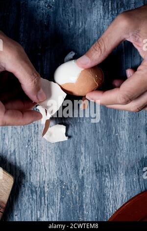 High-Angle-Ansicht eines jungen kaukasischen Mann entfernen die Die Eierschale des gekochten Eies auf dem rustikalen grauen Holz Oberfläche Stockfoto