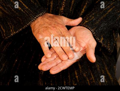 Mann mit dunkelgrüner Chilaba, stellt Zigarettenmund in die Hand, bereitet Haschisch Zigarre mit weißem Rauchpapier, Haschisch Zigarre Vorbereitung Stockfoto