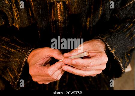 Mann mit dunkelgrüner Chilaba, stellt Zigarettenmund in die Hand, bereitet Haschisch Zigarre mit weißem Rauchpapier, Haschisch Zigarre Vorbereitung Stockfoto