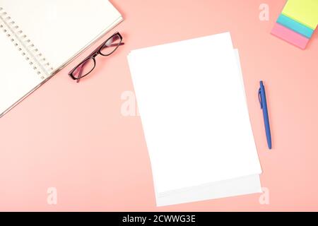 Flaches Lay, Büroschreibtisch von oben. Leeres Papier, Brillen, Notizblock, Notizpapier auf rosafarbenem Tisch. Flacher Schreibtisch für Damen Stockfoto
