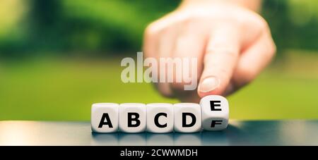 Symbol für Grundunterricht. Die Hand dreht Würfel und korrigiert die Buchstabenfolge von 'a b c d f' auf 'a b c d e'. Stockfoto