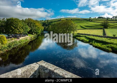 Blick auf den Fluss Wharfe von Burnsall Brücke mit grünen Feldern und blauen Himmel, Yorkshire Dales National Park, Großbritannien Stockfoto