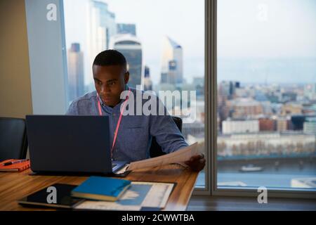 Fokussierter Geschäftsmann, der bei einem Laptop im Hochhausbüro in London, Großbritannien, arbeitet Stockfoto