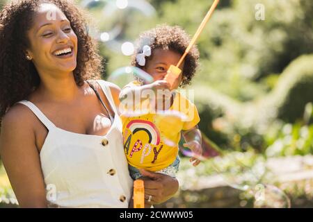 Glückliche Mutter und Kleinkind Tochter spielen mit Blase Zauberstab in Sonnenschein Stockfoto