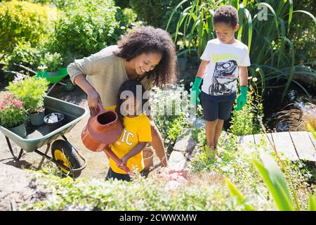 Glückliche Mutter und Kinder Pflanzen im sonnigen Sommergarten gießen Stockfoto