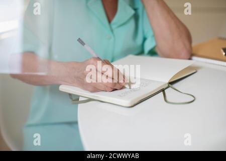 Nahaufnahme einer älteren Frau, die im Tagebuch am Tisch schreibt Stockfoto
