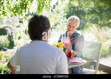 Glückliche ältere Frau Eröffnungsgeschenk von Ehemann auf sonnigen Sommer Terrasse Stockfoto