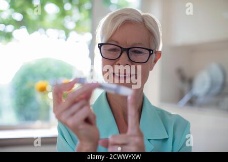 Ältere Frau mit Diabetes mit Blutzuckermessgerät am Finger Stockfoto