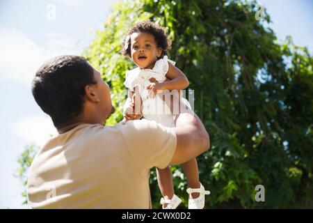 Vater Lifting Kleinkind Tochter Overhead in sonnigen Sommerhof Stockfoto