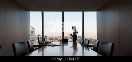 Geschäftsmann, der ein Smartphone am Fenster des Konferenzraums im Hochhaus benutzt Stockfoto