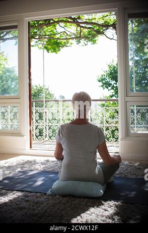 Ruhige ältere Frau, die an der ruhigen Sommerbalkontür meditiert Stockfoto