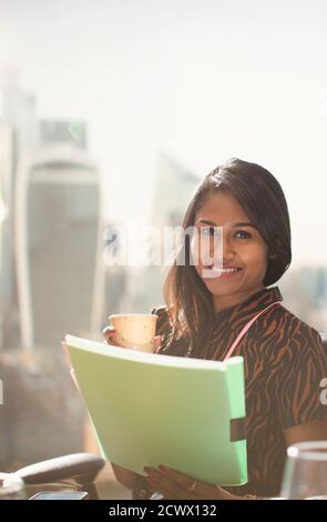 Portrait glückliche Geschäftsfrau mit Papierkram an sonnigen Bürofenster Stockfoto