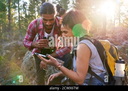 Glückliches junges Wanderpaar mit Smartphone in sonnigen Wäldern Stockfoto