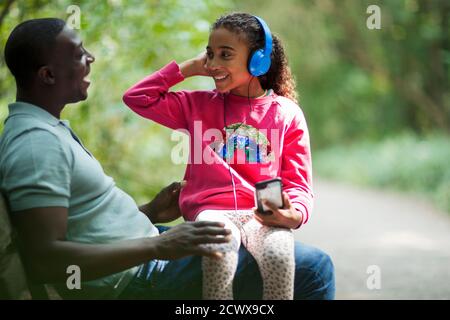 Glücklicher Vater und Tochter sitzen auf Parkbank mit Kopfhörern Stockfoto