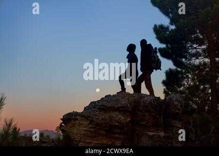 Silhouette junge Wanderer Paar genießen Blick auf den Mond aus dem Fels In der Abenddämmerung Stockfoto