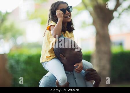 Vater trägt Tochter mit Sonnenbrille auf den Schultern Stockfoto