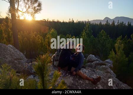 Glücklich anhänglich junges Paar entspannen auf Felsen in Wäldern an Sonnenuntergang Stockfoto
