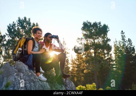 Junges Paar Wandern mit Fernglas auf Felsen in sonnigen Wäldern Stockfoto