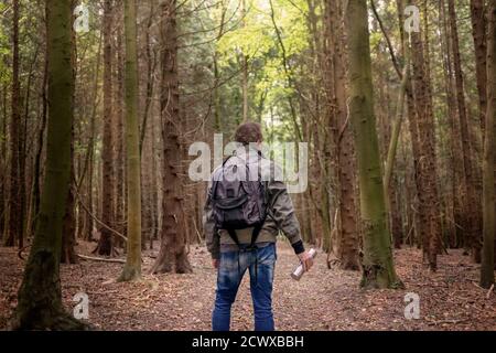 Mann mit Rucksack, der durch einen Wald läuft und eine Metallflasche hält, Rückansicht. Stockfoto