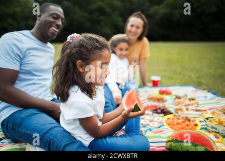 Happy girl essen Wassermelone mit Familie auf Picknick Decke in parken Stockfoto